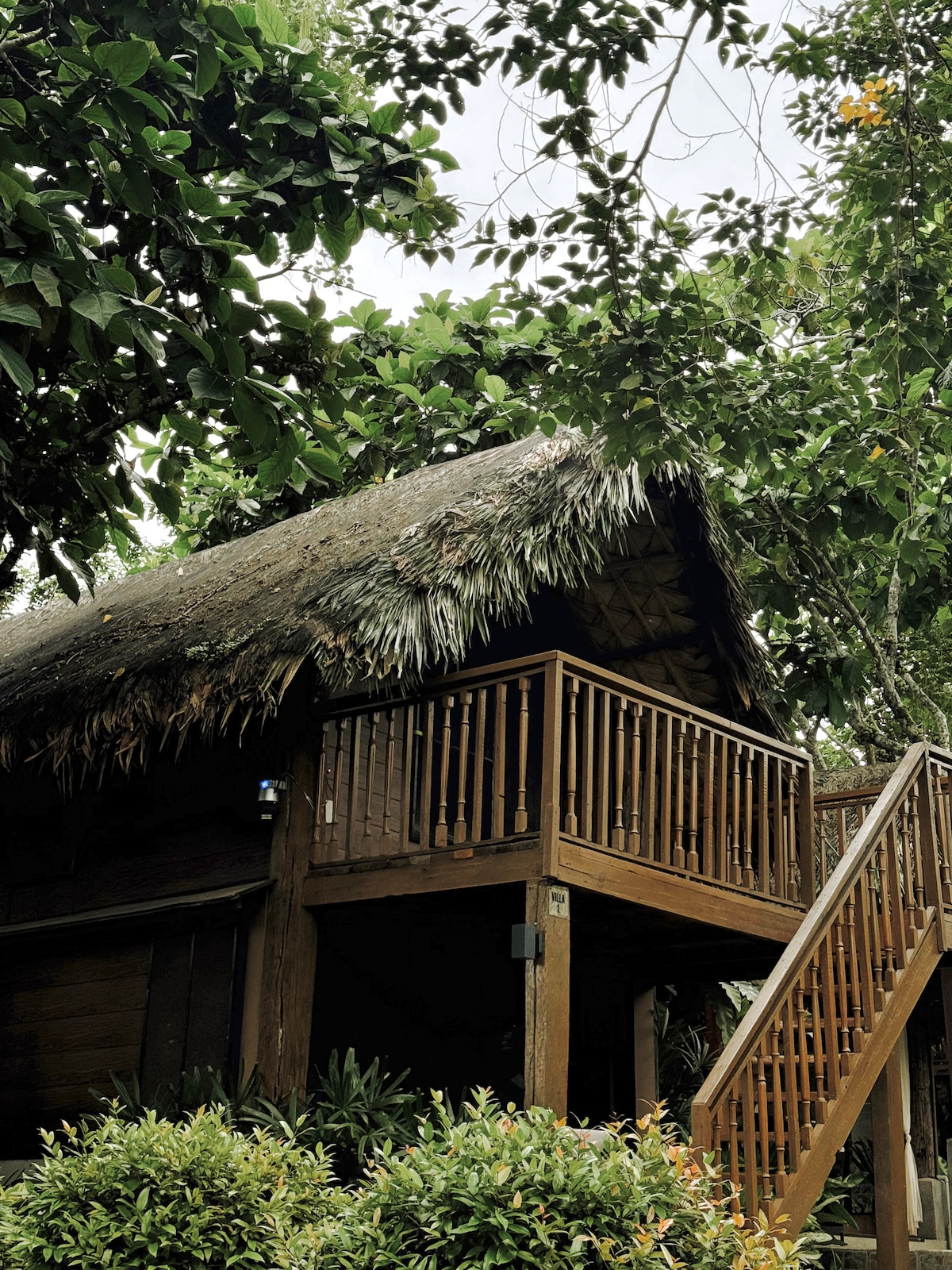 Beladi Villas thatched-roof cabin with wooden staircase surrounded by greenery